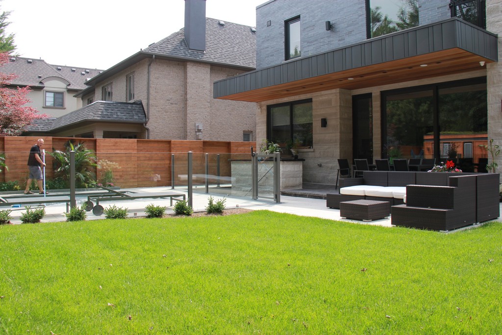 Home renovation project by Milman Design Build, Toronto Home Renovation contractors featuring Back yard landscaping and modern exteriors with outdoor kitchen, interlocking, light fixture, patio and glass railings along pool