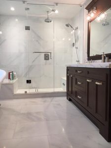 In this image, you can see a renovated bathroom in an Aurora residence, skillfully redesigned by Milman Design Build. It features a sink integrated into a cabinet, a spacious wall mirror, a separate shower area, and a spotless floor.